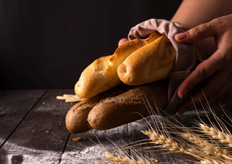 Woman holding tasty fresh bread sorts on a dark Woman holding tasty fresh breads on a dark. Baking and cooking concept background. Hands of baker carefully hold loaf on wooden table, sprinkled with flour.